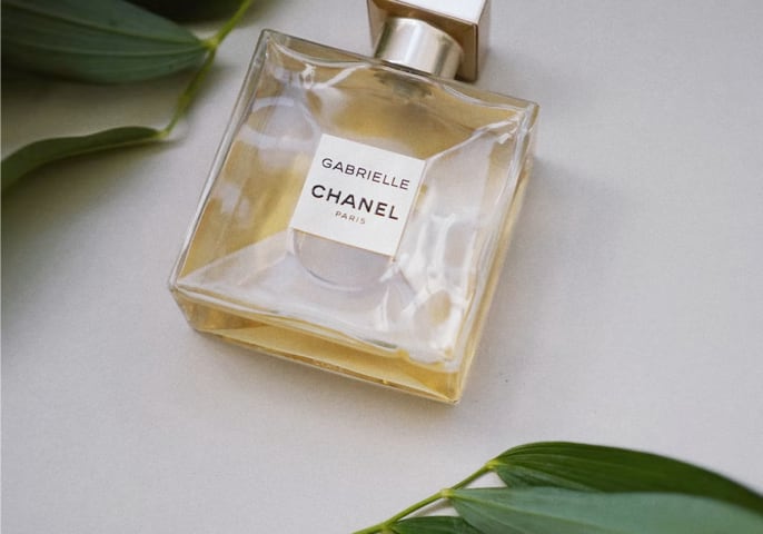 chanel perfume bottle lying on its back between two branches with green leaves 